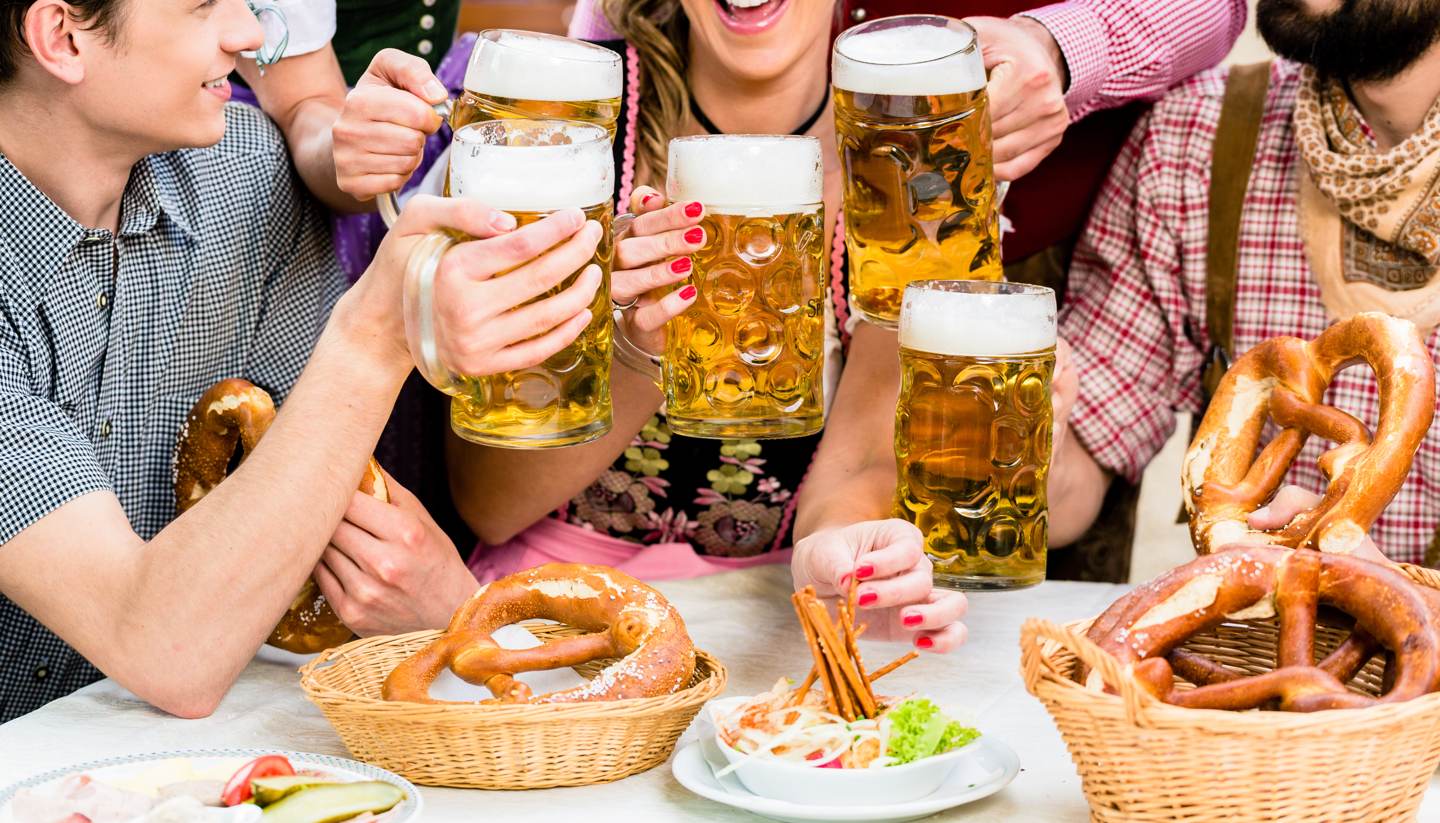 An essential (and fun) guide to Oktoberfest - Friends wearing lederhosen and dirndl drinking beer in a beer garden
