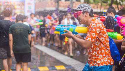 Man in Floral orange shirt and pink goggles shooting water at someone at Songkran