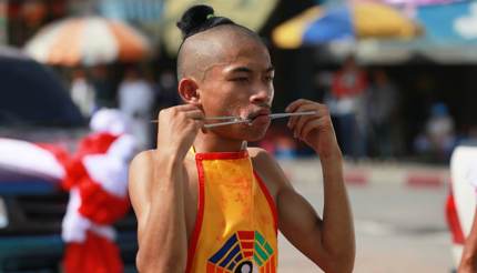 Young man with two thin metal rods going through his cheeks at Phuket Vegetarian Festival