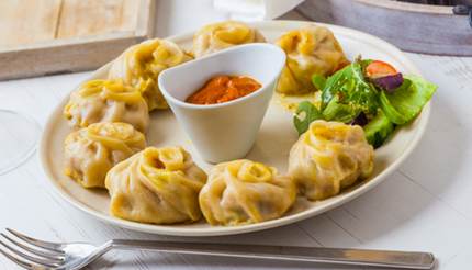 Plate of momos with tomato chutney in a dip bowl in the middle